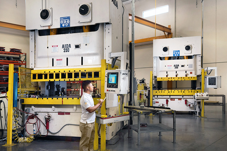 Person inspecting process of two large sheet metal stamping machines