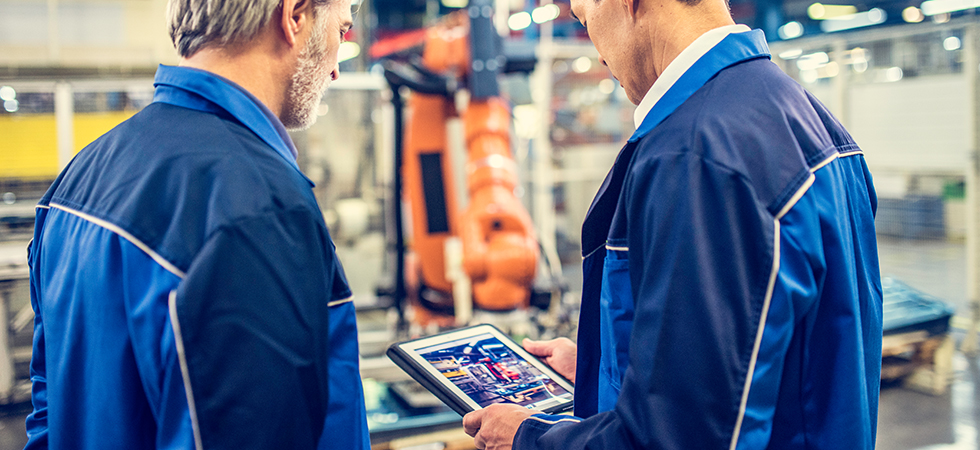 Two employees monitoring industrial equipment on a tablet computer